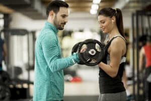young woman being guided by her personal trainer on how to properly perform a bicep curl